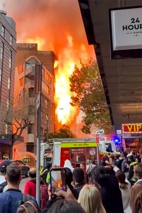 This screen grab from a UGC video taken and posted by Grant Ozolins on the Twitter account @grantozolins on May 25, 2023 shows people watching a fire in central Sydney. More than 100 firefighters battled towering flames and thick smoke from a seven-storey blaze in central Sydney on May 25 that was spreading to other buildings. (Photo by Grant OZOLINS / Twitter/@grantozolins / AFP) / -----EDITORS NOTE --- RESTRICTED TO EDITORIAL USE - MANDATORY CREDIT 