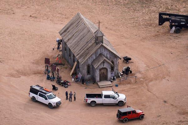 An aerial photo of the movie set of Rust, showing a wooden church with camera equipment, trucks and people outside.